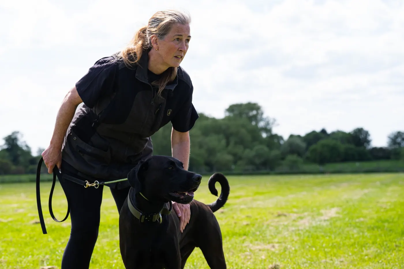 Caroline crouching beside Ralph on a lead in a sunny field (photo: Jake @reelestK9)
